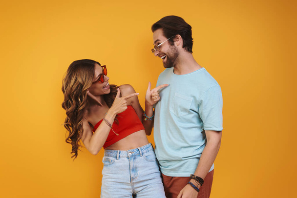 Beautiful young couple in eyeglasses having fun while standing against yellow background - Foto, Bild