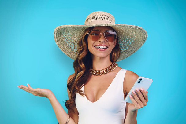 Happy young woman in elegant hat holding mobile phone and looking at camera - Valokuva, kuva