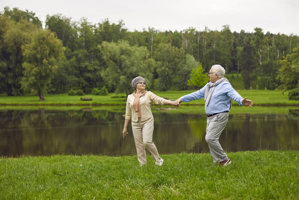 Happy senior couple taking a stroll by the river in a green park on a nice summer day - Fotoğraf, Görsel