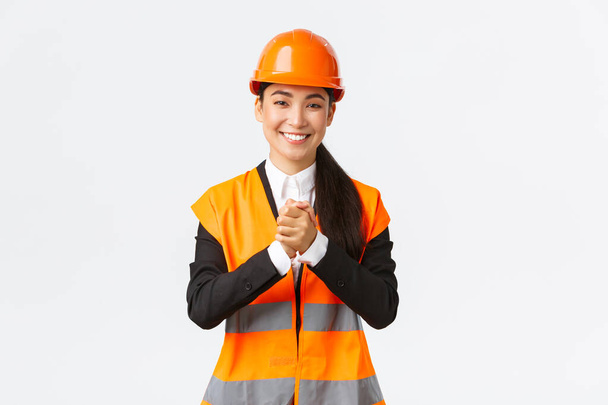 Une femme architecte asiatique reconnaissante salue les investisseurs ou les clients dans la zone de construction, portant un casque et une veste de sécurité, serrant les mains serrées en reconnaissance, reconnaissant pour la confiance - Photo, image