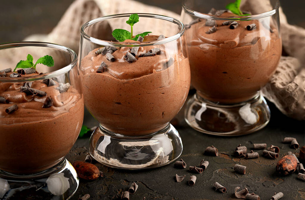 Mousse de chocolate vegano con menta, barra de chocolate y granos de cacao sobre un fondo oscuro. Copiar espacio - Foto, imagen