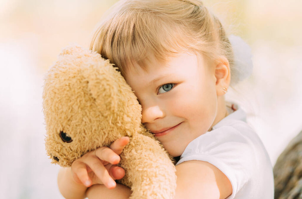 Little girl blonde hugs a soft toy bear - Foto, afbeelding