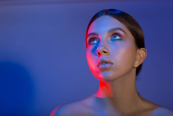 Portret van jonge mooie positieve vrouw met naakt make-up en kleurrijk licht - Foto, afbeelding