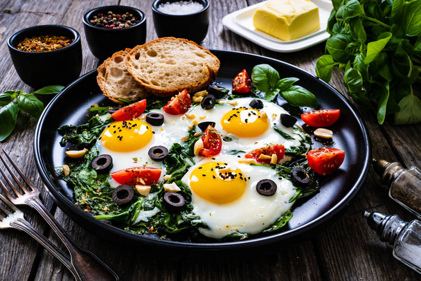 Sunny side up eggs with spinach, cherry tomatoes and black olives on wooden table  - Foto, afbeelding