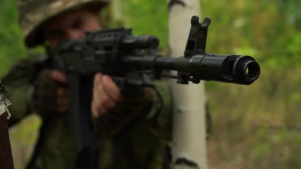 soldaat mikt met een machinegeweer, kijkt uit van achter een boom in het bos - Video