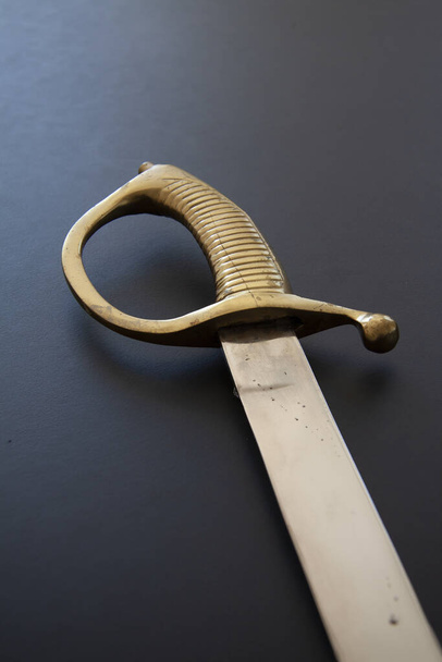 A vertical closeup of an old fashioned sword on a black surface - Φωτογραφία, εικόνα