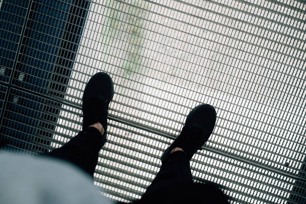 A high angle shot of male legs with black trousers and shoes standing on a metal grid - Zdjęcie, obraz