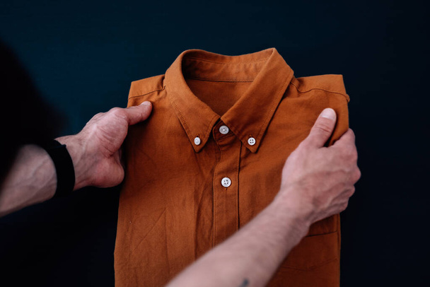 A male folding an orange shirt on the table - Fotoğraf, Görsel