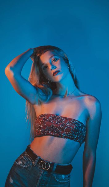 A seductive young Spanish female wearing a sexy top posing in a studio in blue neon lights - Foto, imagen