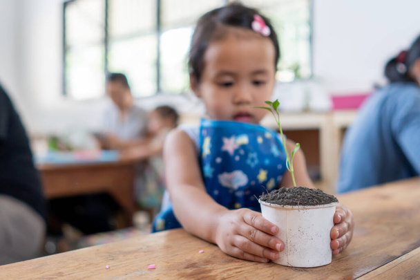 A closeup shot of a Southeast Asian baby girl staring at the plant - Foto, Imagem