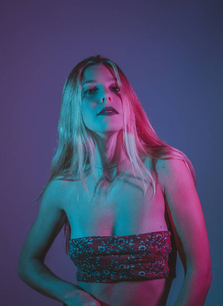 A seductive young Spanish female wearing a sexy top posing in a studio in blue and purple neon lights - Zdjęcie, obraz