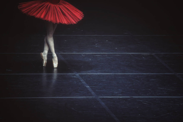 A ballerina wearing a red dress and performing on the dark stage - Foto, afbeelding