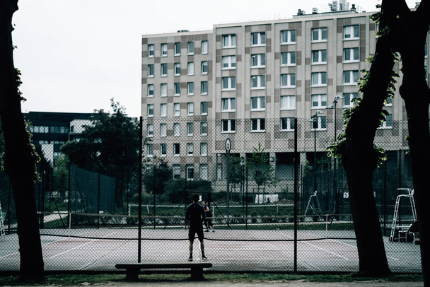 The two people playing in the tennis court near the residential building on a gloomy day - Foto, afbeelding