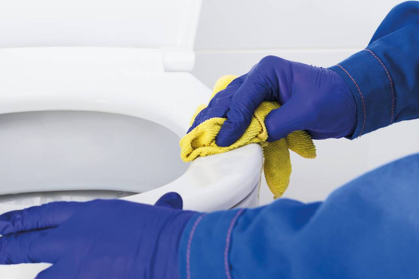 een medewerker van een schoonmaakbedrijf is de rand van de toiletpot aan het schoonmaken en wassen, close-up - Foto, afbeelding
