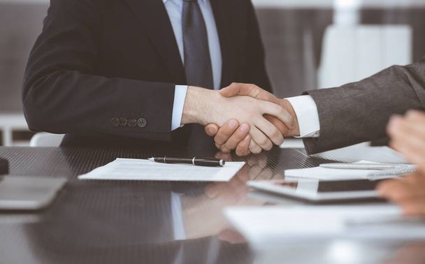 Handdruk als succesvol onderhandelingsresultaat, close-up. Onbekende zakenmensen schudden elkaar de hand na het tekenen van een contract in een modern kantoor - Foto, afbeelding