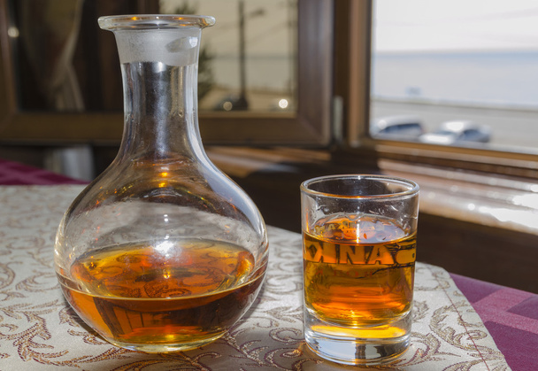 Vodka de cedro en un vaso y jarra contra la ventana con vistas al lago Baikal
 - Foto, Imagen