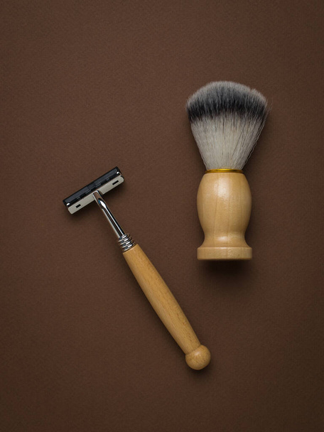 Cepillo de afeitar y maquinilla de afeitar con mango de madera sobre fondo marrón. Accesorios para hombre para el cuidado de la apariencia. Puesta plana. - Foto, imagen