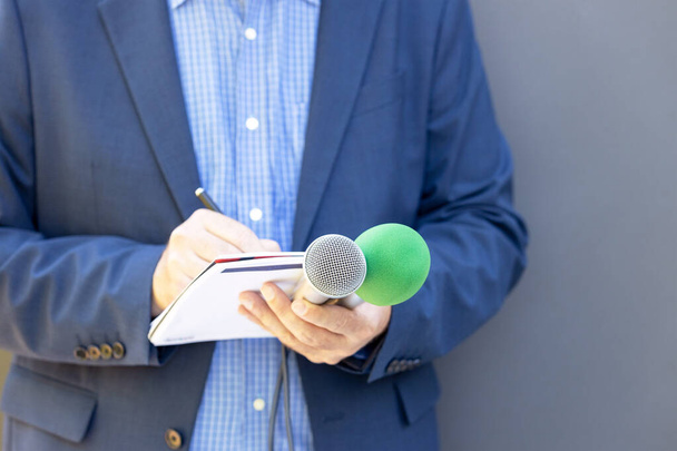 Journalist at news conference or media event, holding microphone, writing notes. Broadcast journalism concept. - Foto, Imagen