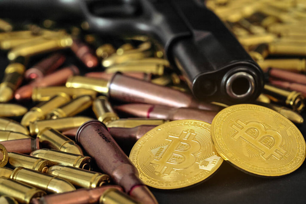Bronze and brass gun bullets scattered on dark table, black pistol barrel, golden bitcoin coins near - illegal use of cryptocurrency to purchase weapon concept - Zdjęcie, obraz