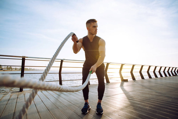 Young man wearing sports clothes is doing exercisesat the beach pier in the morning. Battle ropes. Kettlebell. Sport, Active life. - Foto, Bild