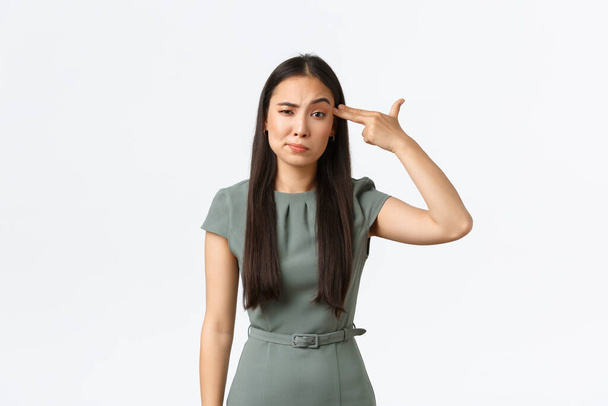 Small business owners, women entrepreneurs concept. Annoyed and tired asian businesswoman, employee shooting herself with fake gun gesture in head as fed up, standing white background - Photo, Image