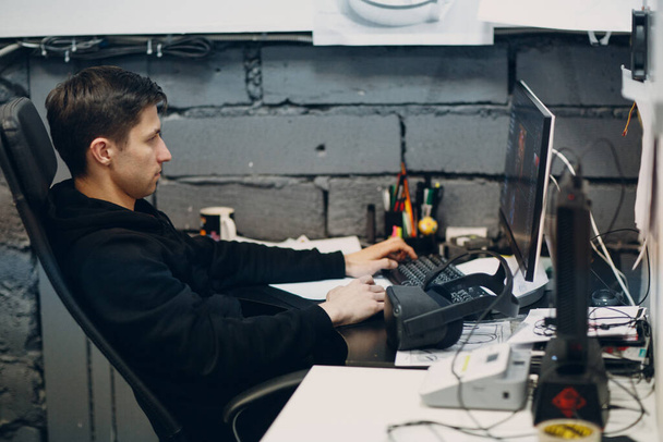 Jongeman programmeur gamer zitten op stoel met computer desktop in de buurt van virtual reality bril, vr bril headset - Foto, afbeelding