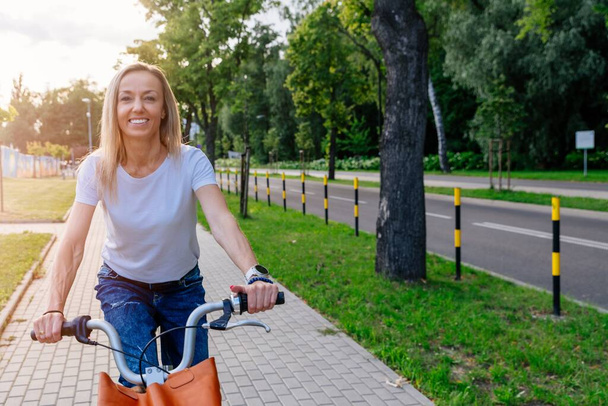 Eine hübsche junge Frau im weißen T-Shirt fährt ein Stadtrad. - Foto, Bild