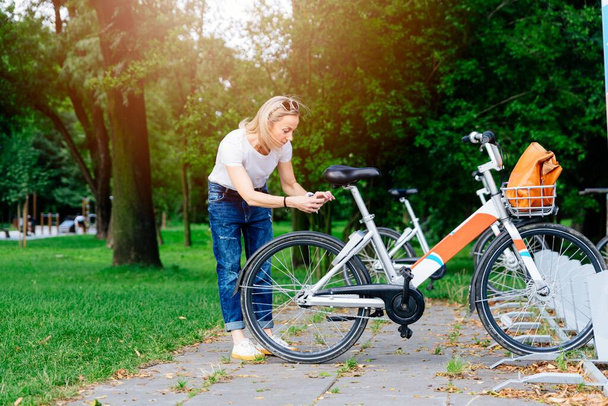Femme heureuse prenant vélo via des services de location de vélos dans le centre-ville. - Photo, image