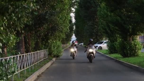 Twee jonge vrouwen in beschermende helmen langzaam rijden motorfietsen op smalle weg - Video