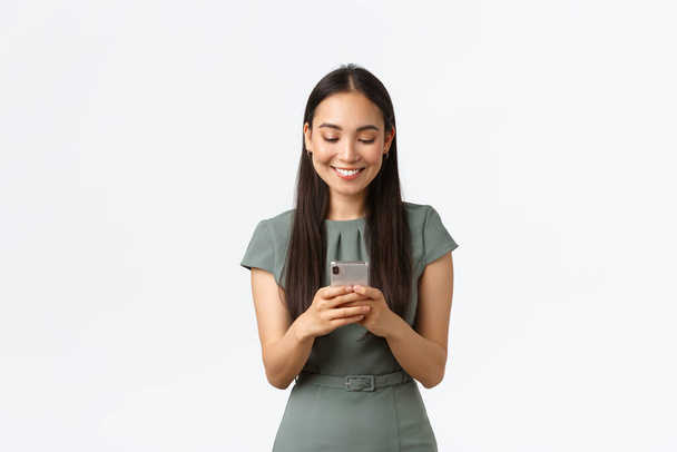 Small business owners, women entrepreneurs concept. Smiling young female running startup in internet, checking messages from clients, texting someone on mobile phone, using smartphone - Fotó, kép
