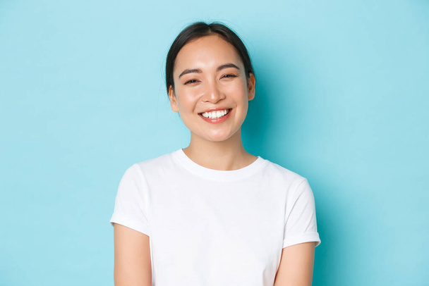 Крупним планом весела безтурботна азіатська дівчина в білій футболці посміхається широко. Приємна корейська жінка виглядає доброзичливо на камеру, насолоджується приємною розмовою, розмовляє з кимось, світло-блакитний фон
 - Фото, зображення