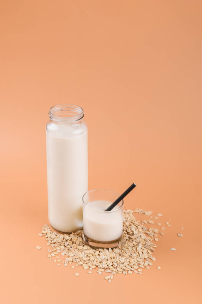 Oat milk in bottle and glass on the oat flake on pastel peach color background - Foto, Imagem