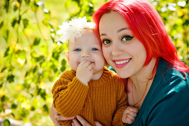 赤い髪と魅力的な赤ちゃんを持つ女性の大きな肖像画。母と娘は一緒に晴れた秋の日を楽しむ. - 写真・画像