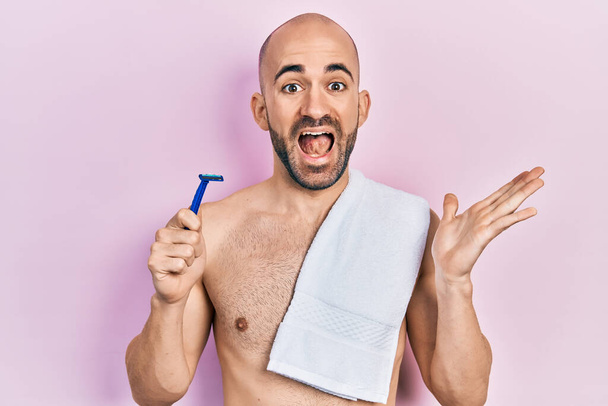Young bald man shirtless holding razor celebrating achievement with happy smile and winner expression with raised hand  - Photo, Image