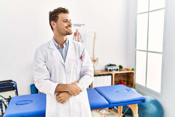 Hezký mladý muž pracující na klinice pro zotavení bolesti, dívající se stranou s úsměvem na tváři, přirozený výraz. jistota smíchu.  - Fotografie, Obrázek