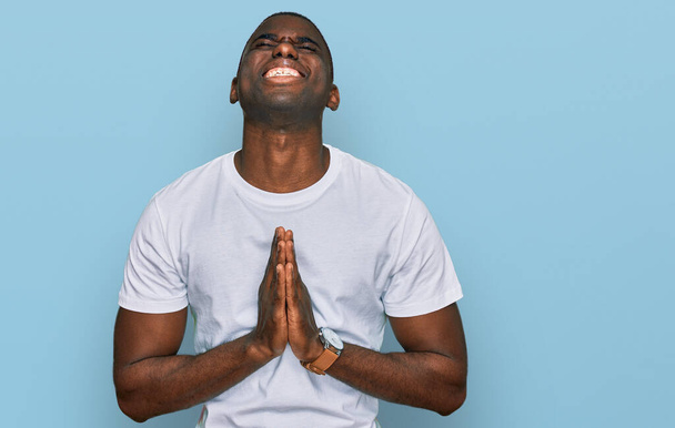 Young african american man wearing casual white t shirt begging and praying with hands together with hope expression on face very emotional and worried. begging.  - Foto, Imagen