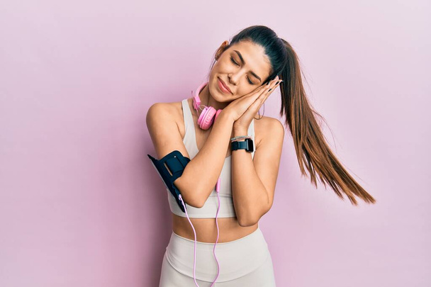 Молода іспаномовна жінка носить спортивний одяг і використовує навушники сплячі втомлені сни і позує руками разом, посміхаючись закритими очима
.  - Фото, зображення