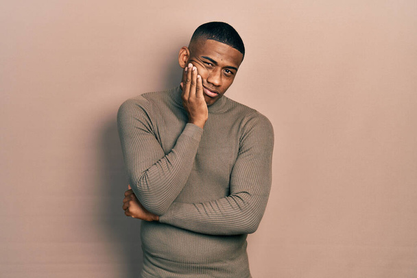 Fiatal fekete férfi visel alkalmi garbó pulóver gondolkodás fáradt, és unatkozik a depresszió problémák keresztbe karok.  - Fotó, kép