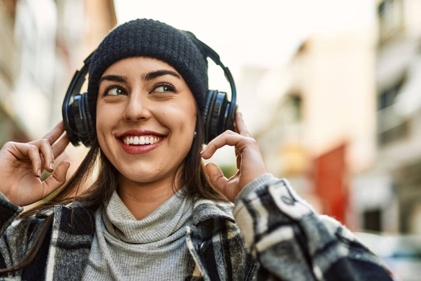 Joven mujer hispana sonriendo feliz usando auriculares en la ciudad. - Foto, Imagen