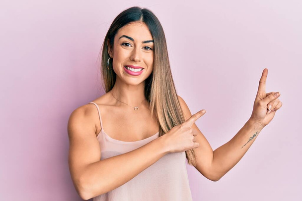Young hispanic woman wearing casual sleeveless t shirt smiling and looking at the camera pointing with two hands and fingers to the side.  - Photo, Image