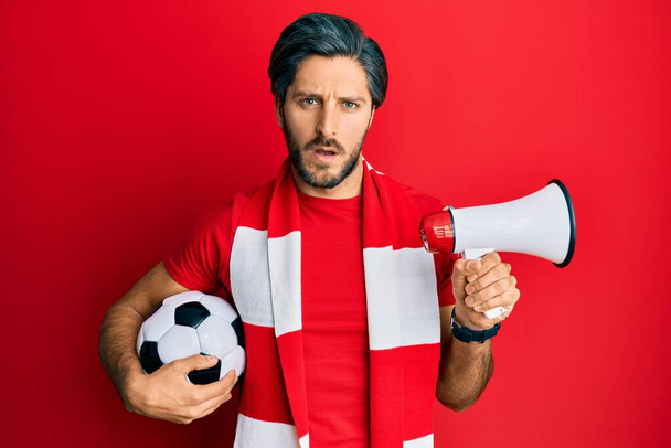 Genç İspanyol futbolcu holigan topu elinde tutuyor. Şok suratlı megafon kullanıyor. Şüpheci ve alaycı görünüyor.  - Fotoğraf, Görsel
