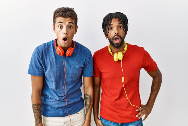Young hispanic brothers standing over isolated background wearing headphones afraid and shocked with surprise expression, fear and excited face.  - Photo, image
