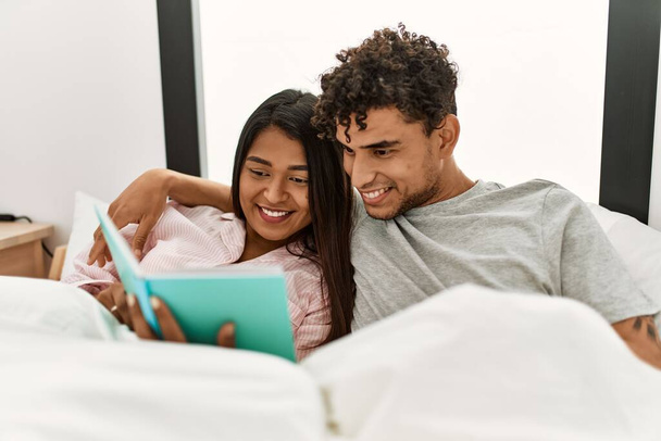 Yatak odasındaki yatakta kitap okuyan genç Latin çift.. - Fotoğraf, Görsel