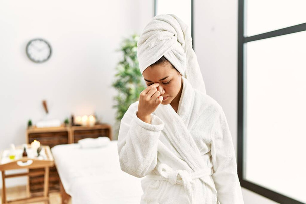 Young brunette woman wearing towel and bathrobe standing at beauty center tired rubbing nose and eyes feeling fatigue and headache. stress and frustration concept.  - Fotó, kép