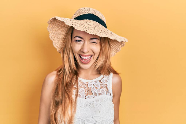 Young caucasian woman wearing summer hat winking looking at the camera with sexy expression, cheerful and happy face.  - Foto, Bild
