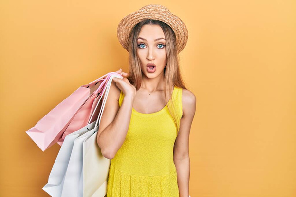 Young blonde girl holding shopping bags scared and amazed with open mouth for surprise, disbelief face  - Fotografie, Obrázek