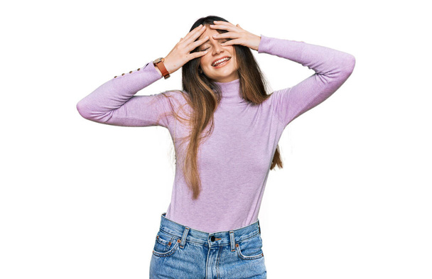 Young beautiful teen girl wearing turtleneck sweater covering eyes with hands smiling cheerful and funny. blind concept.  - Foto, afbeelding