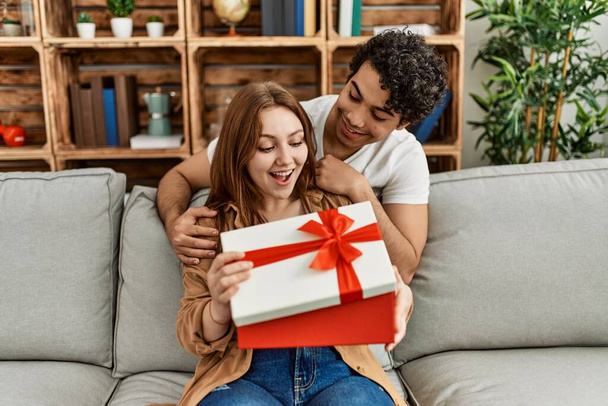 Young couple smiling happy sitting on the sofa surprise with anniversary gift at home. - Foto, Bild