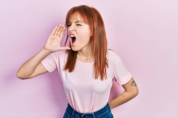 Rudowłosa, młoda kobieta w różowej koszulce krzycząca i krzycząca głośno, by stanąć z ręką w twarz. Koncepcja komunikacji.  - Zdjęcie, obraz
