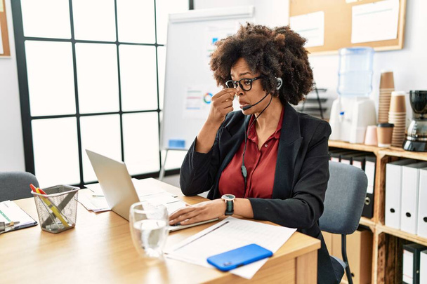 Afrikai amerikai nő afro haj dolgozik az irodában visel kezelő headset fáradt dörzsölés orr és szem érzés fáradtság és fejfájás. stressz és frusztráció fogalma.  - Fotó, kép